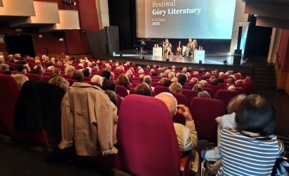 Wypełniona widownia kinoteatru, na scenie dyskusja trzech osób, za nimi na dużym ekranie napis Góry Literatury