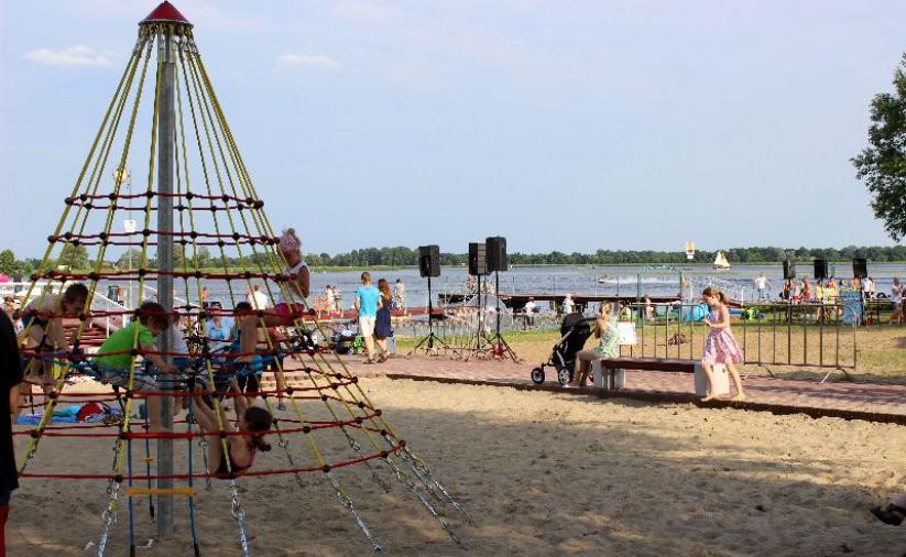 Plaża piaszczysta przy Zalewie Zegrzyńskim, na pierwszym planie dzieci bawiące się na placu zabaw