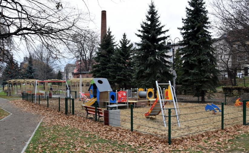 Widok na ogrodzony plac zabaw, na drugim planie drzewa