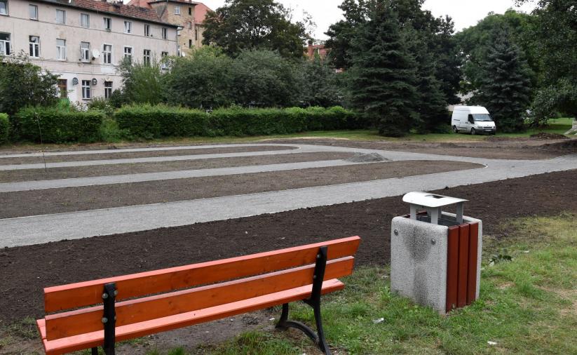 Nowa łąwka i kosz na śmieci, w tle miejsce na owocowy skwer