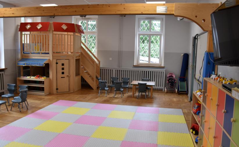 Sala zabaw z kolorową matą na podłodze i drewnianym domkiem w drugim planie