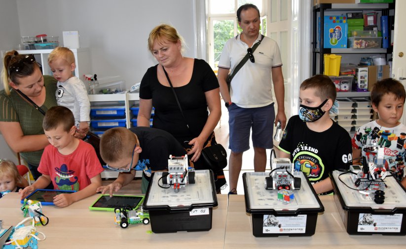 Grupa dorosłych i dzieci prszy stołach z miniaturowymi robotami