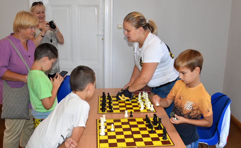 Stół z rozłożonymi szachami i grupą młodzieży dookoła