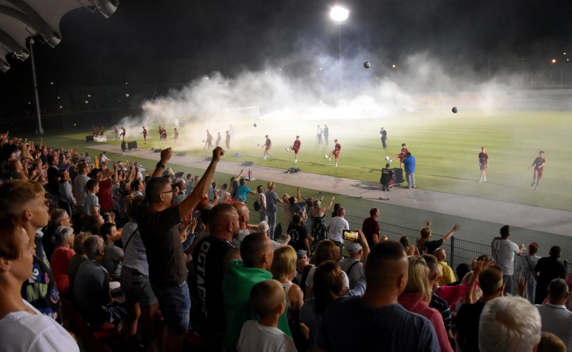 Stadion nocą, pełna trybuna kibiców, na boisku piłkarze 