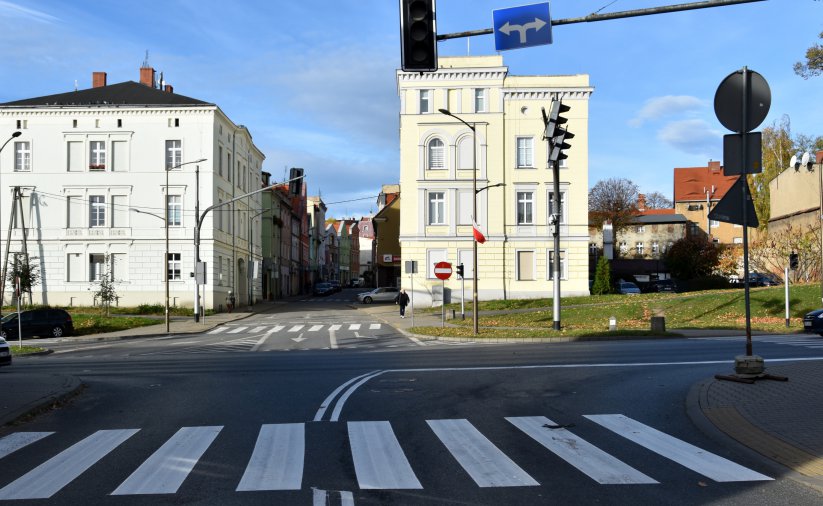 Skrzyżówanie dróg w mieście, na pierwszym planie przejście dla pieszych na drugim dwie kamienice