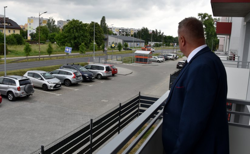 Mężczyzna stojący na balkonie i patrząacy na parking przed budynkiem