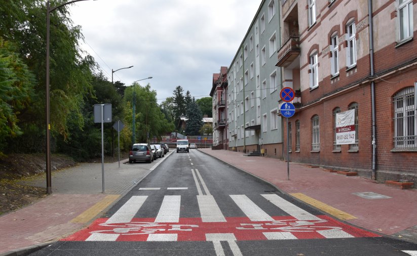 Przejście dla pieszych z przejadem dla rowerów, po prawej stronie drogi kamienice, po lewej drzewa