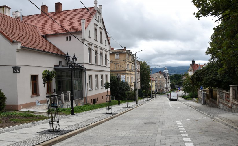 Kamienica z patelową elewacją, droga, po drógiej stronie zieleń drzew