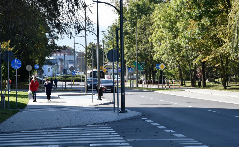 Piesi idący chodnikiem, bok droga i miejsca postojowe 