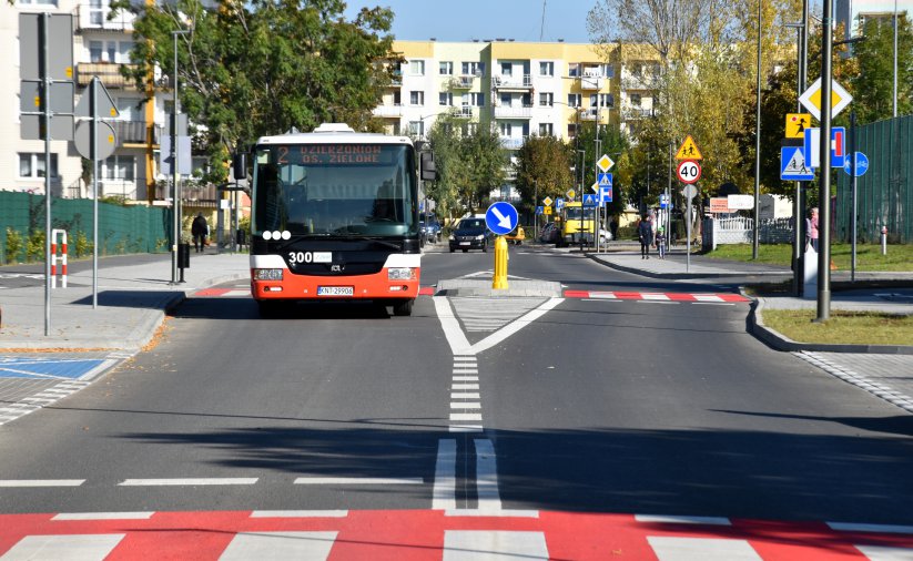 Autobus komunikacji miejskiej jadący po osiedlowej drodze, w tle bloki mieszkalne