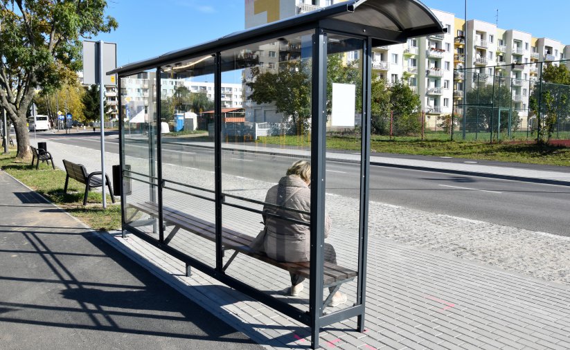 Przystanej autobusowy, osoba siedząca na ławce w tle długi czteropiętrowy blok