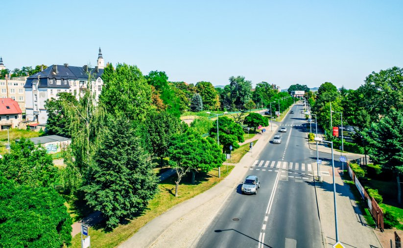 Prosta droga przebiegająca przez miasto, po bokach zieleń