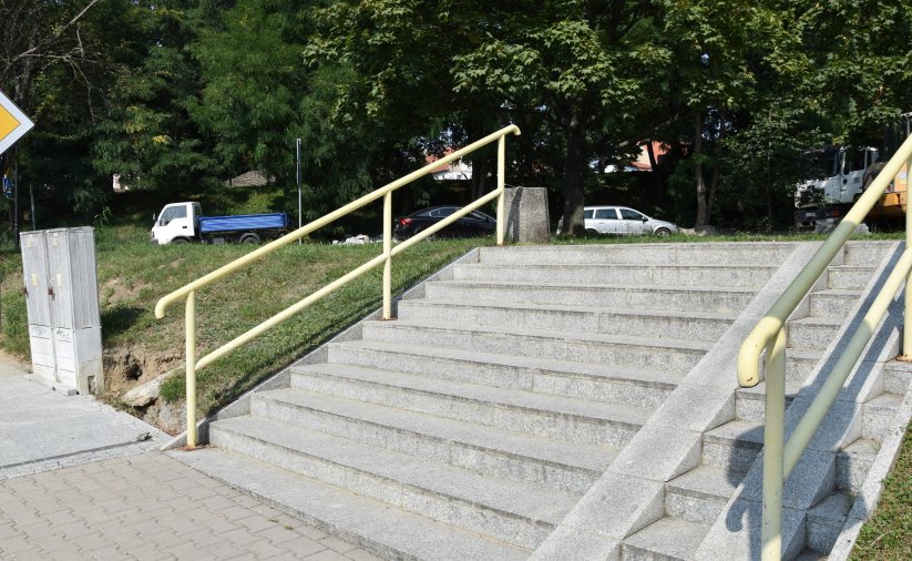 Kamienne schody, po bokach żółte poręcze w tle park