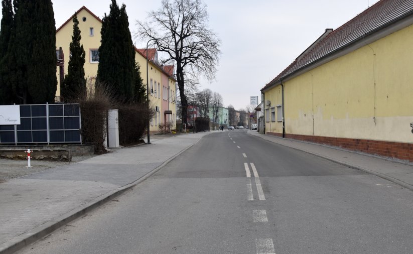 Droga miejska, po prawej niski żółty budynek, po lewej zieleń