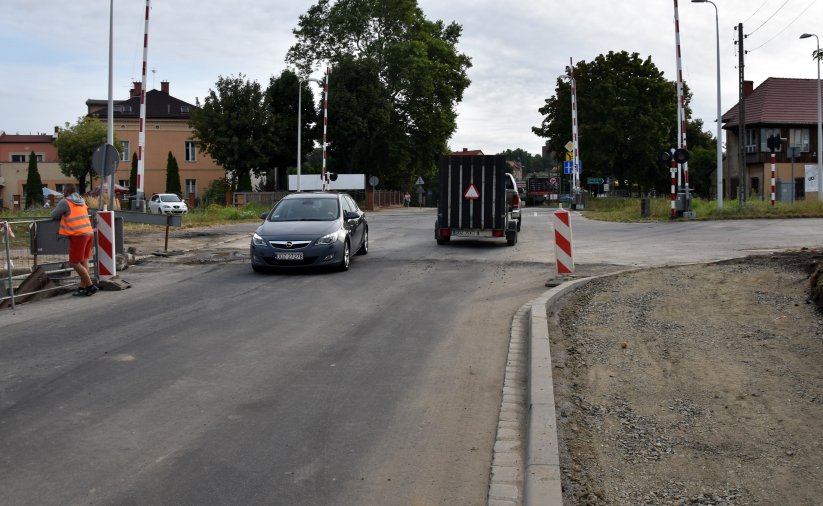 Samochody przejeżdżające przez tory, w tle budynki