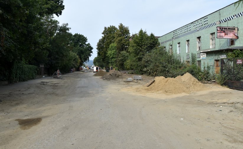 Remontowana droga z odsłonięta podbudową, po bokach drzewa i zielony budynek
