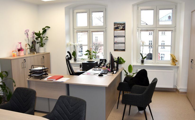 dwa ustawione naprzeciw siebie biurka, w tle okna