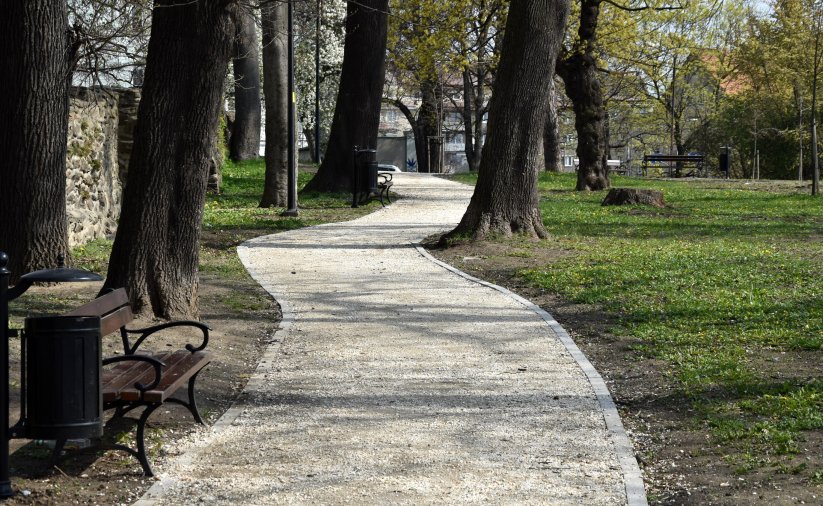 Chodnik, obok ławka, po prawej zieleń, po lewej mury kamienne