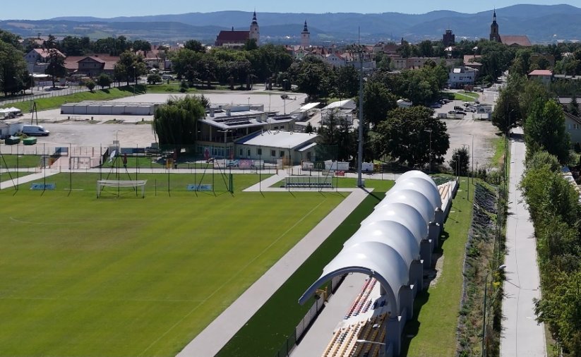 Boisko do piłki nożnej, zadaszone trybuny, za nimi chodnik
