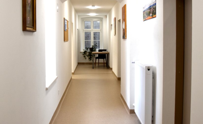 Korytarz, białe ściany, na końcu stolik i krzesło