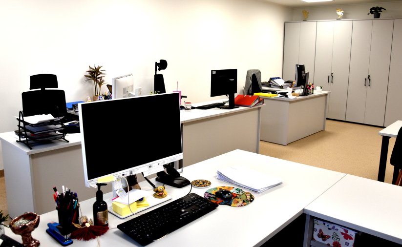 Duże biurko, na nim komputer, na drugim planie dwa biurka i szafy
