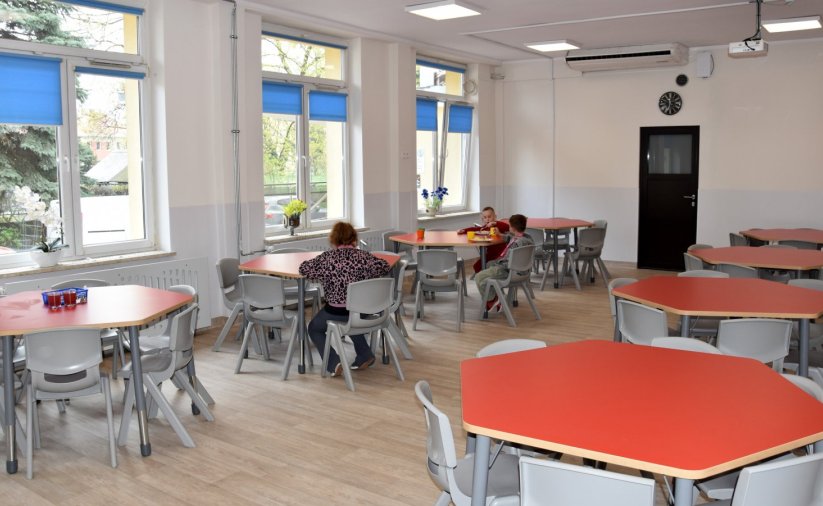 Sześciokątne stoły przy jednym troje uczniów jedzących obiad