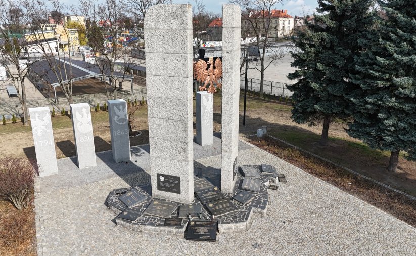 Plac z kostki, pomnik w postaci dwóch kolumn, między nimi duże godło