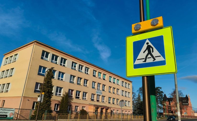 Znak drogowy z mężczyzną przechodzącym przez pasy, w tle budynek