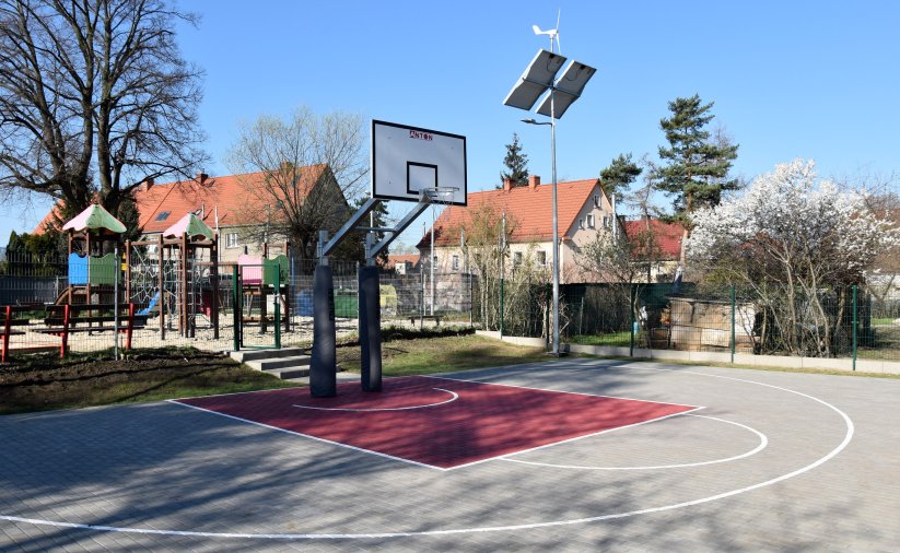 Boisko do kosza z kostki maiennej, za nim plac zabaw