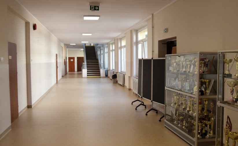 Korytarz szkolny, przy ścianie gablota ze złotymi pucharam