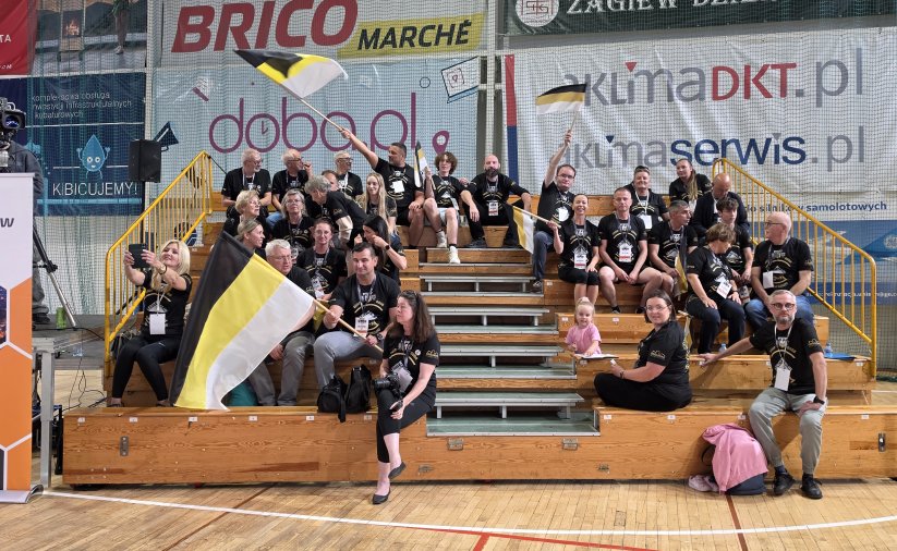 Piętrowa trybuna w hali sportowej wypełniona kibicami w czarnych koszukach