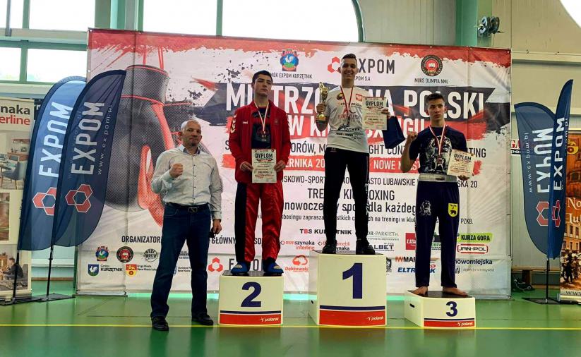 Maksymilian Palej na najwyższym stopniu podium, obok inni zawodnicy i trenerzy