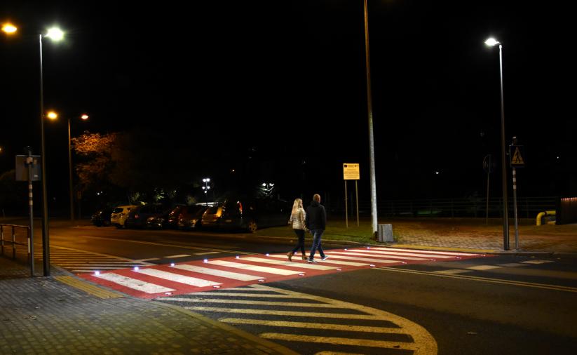 Dobrze oświetlone przejscie dla pieszych, przez które przechodzi para mieszkańców