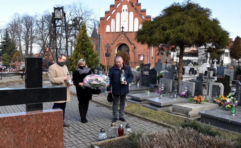 Trzy osoby składają wiążankę kwiatów przy pomniku na dzierżóniowskim cmentarzu 