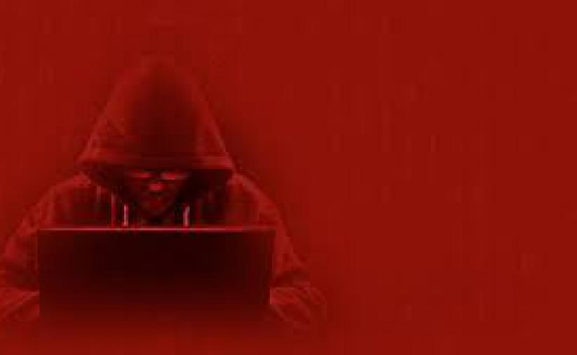 Czerwone tło, w drugmi planie osoba przed komputerem zakryta kapturem