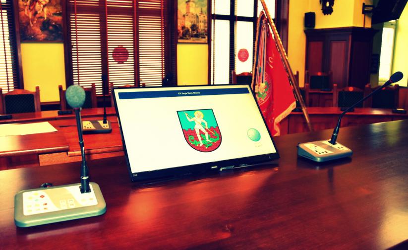 Stół prezydialny, na nim monitor z herbem Dzierżoniowa