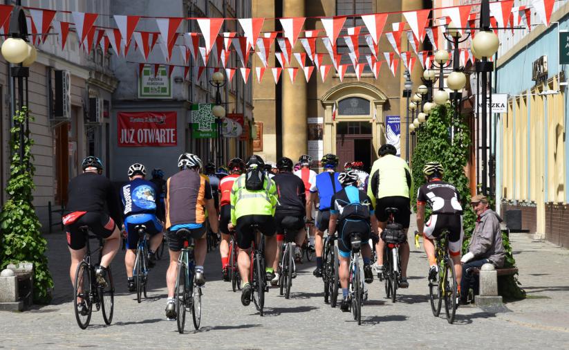 Grupa rowerzystów jadąca ulicą, po bokach kamienice