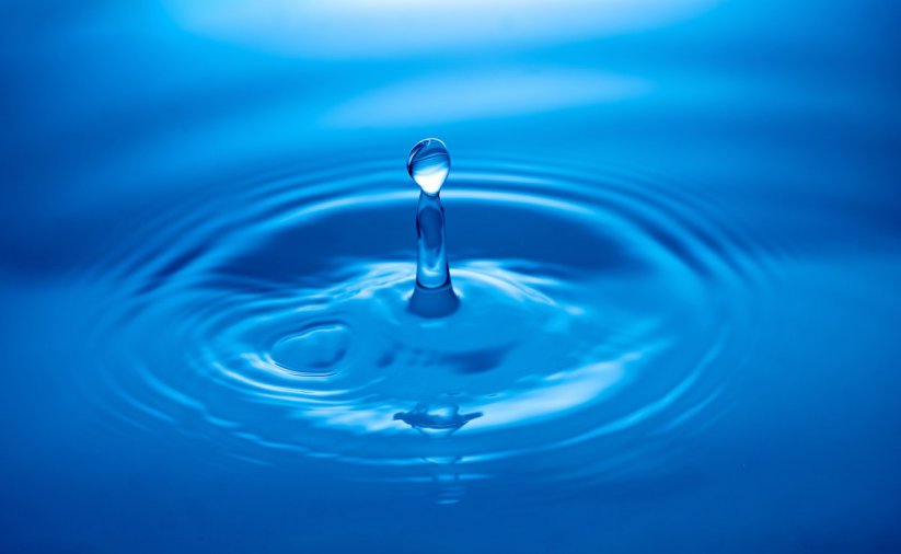 Kropla spadająca na taflę wody, niebieskie tło