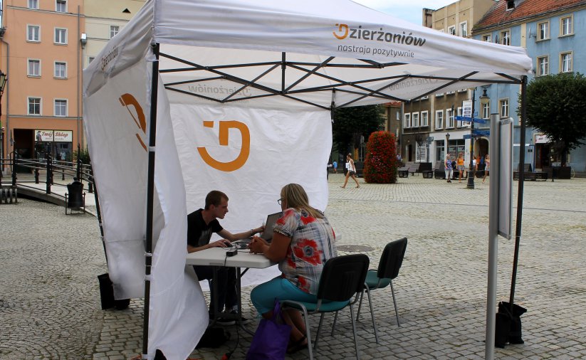 Biały napmiot z logiem Dzierżoniowa, w nim dwie osoby przy stole