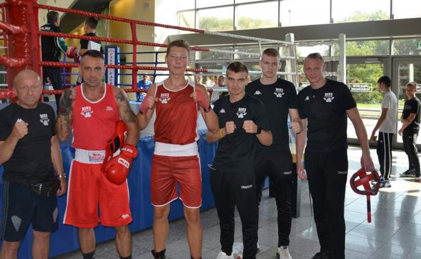 Grupa zawodników i trenerów stojąca rzed ringiem bokserskim 