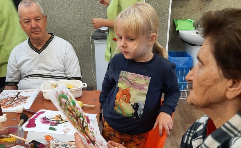 Na zdjęciu dzieci i seniorzy razem wykonują prace plastyczne