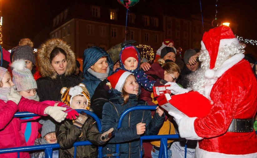 Mikołaj otoczony dziećmi rozdaje prezenty. Noc.