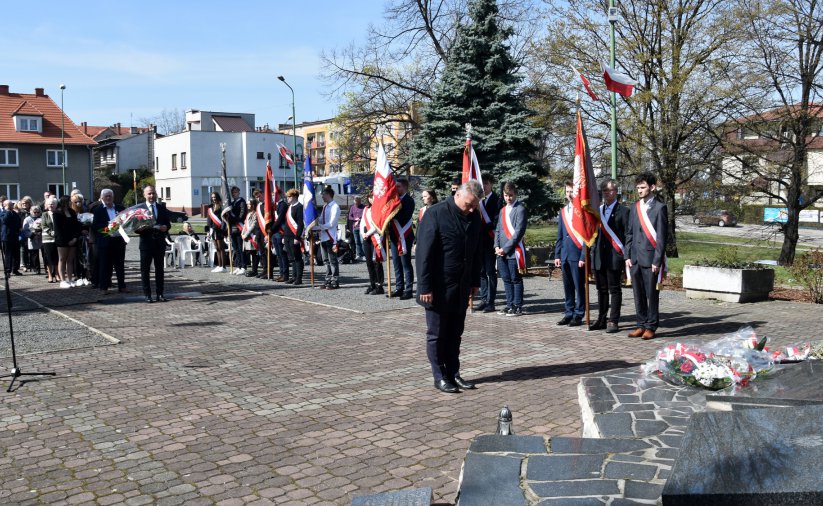 Mężczyzna stojący przed pomnikiem, w durim tle poczet sztandarowy