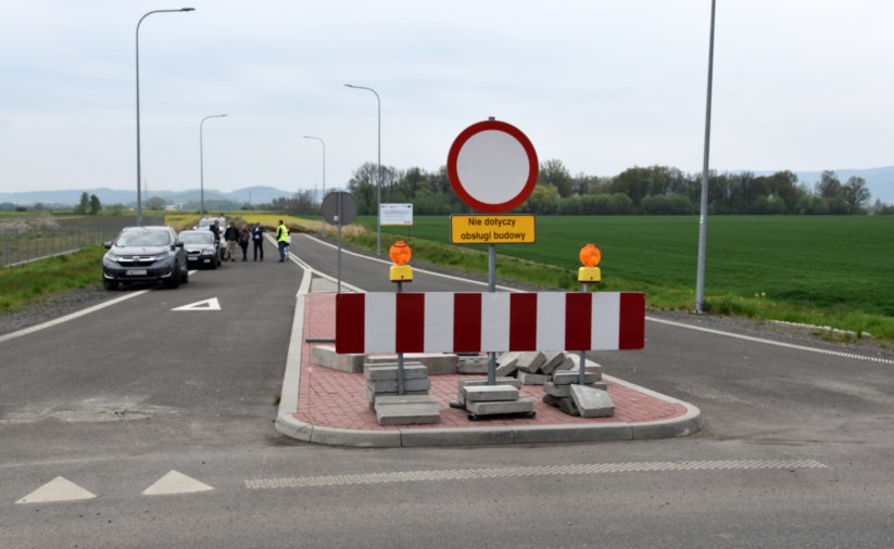 Droga ze znakiem zakazu wjadu zagrodzona barierką, w drugim planie grupka ludzi