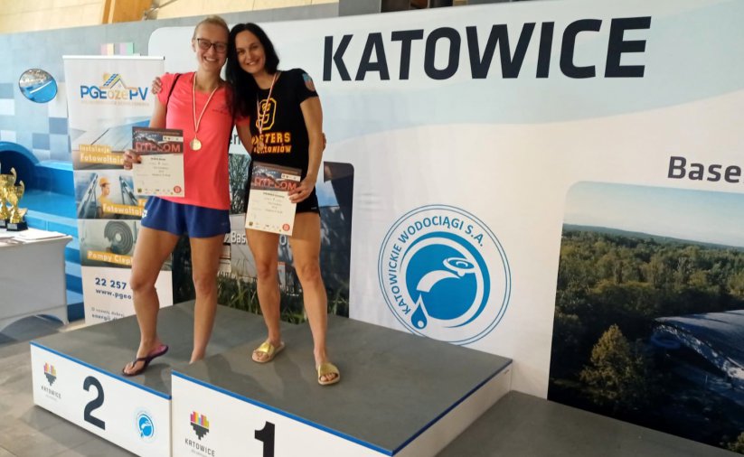 Dwie uśmiechnięte zawodniczki na podium, obok napis Katowice