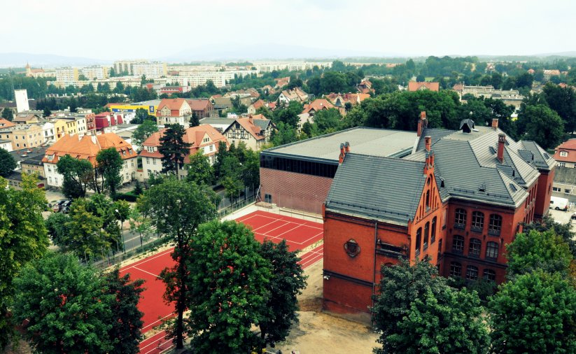 Fragment miasta z góry, na pierwszym planie duży budynek z cegły i boisko 