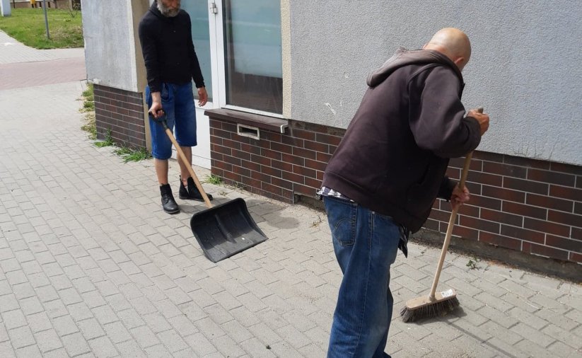 dwóch mężczyzn zamiata chodnik przed budynkiem