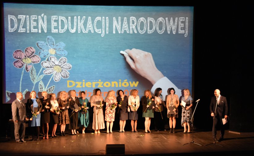 Grupowe zdjęcie nauczycielek na scenie, z tyłu grafika z napisem Dzień Edukacji