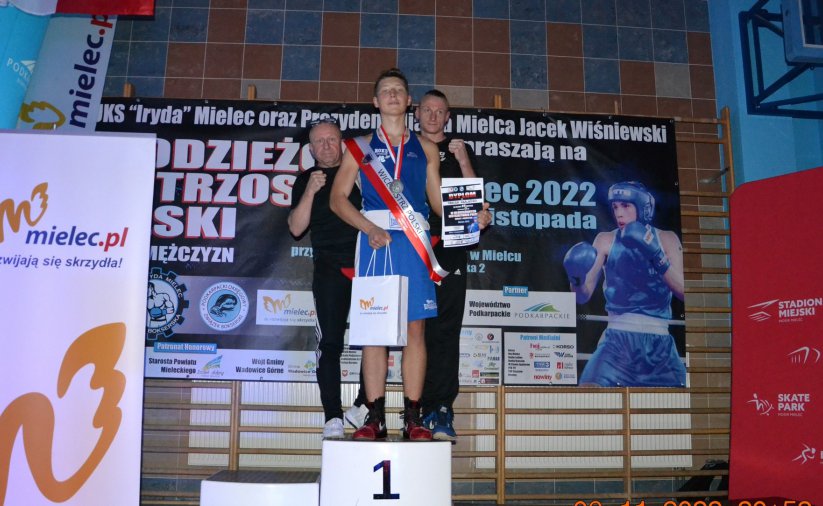 Zawodnik stojący na podium, za nim dwóch trenerów