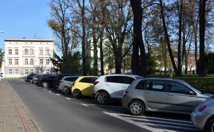 Ulica w mieście, po prawej zaparkowane auta, w drugim planie duża kamienica